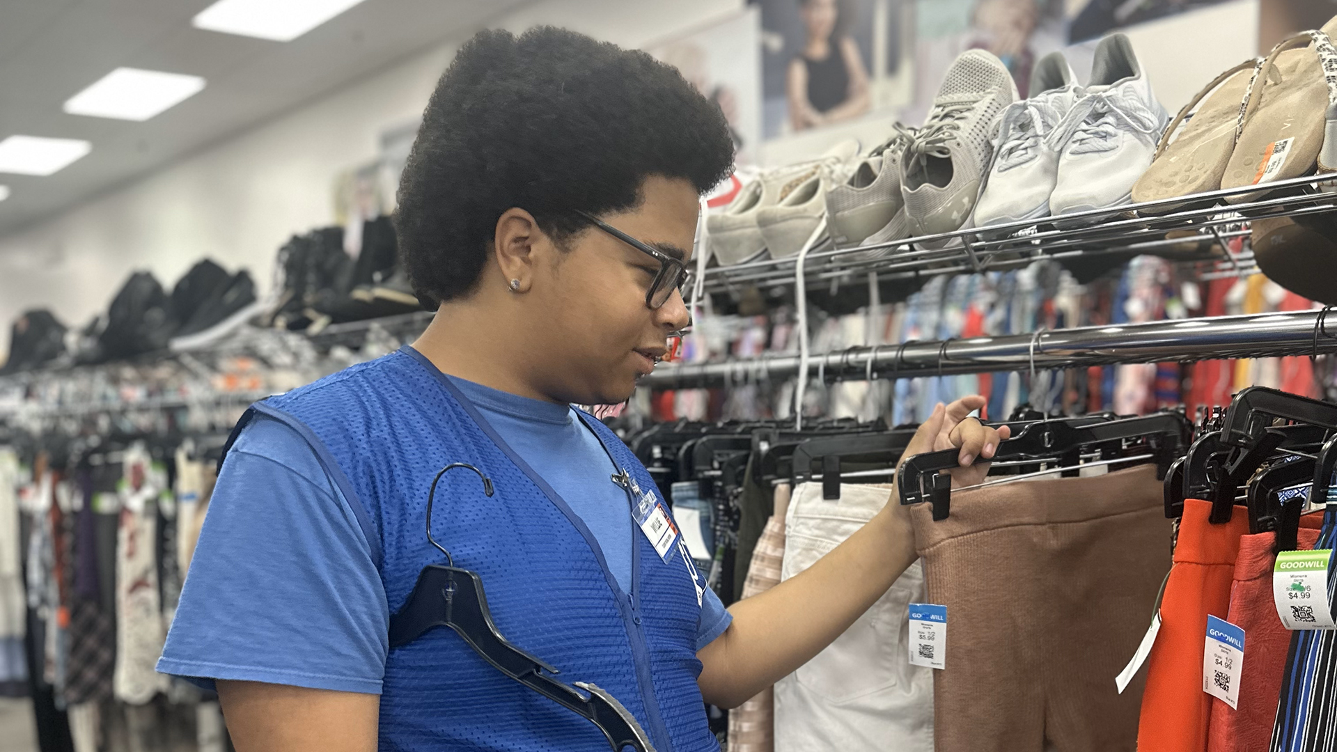 An African American youth boy wearing a blue shirt checks inventory at a retail clothing store