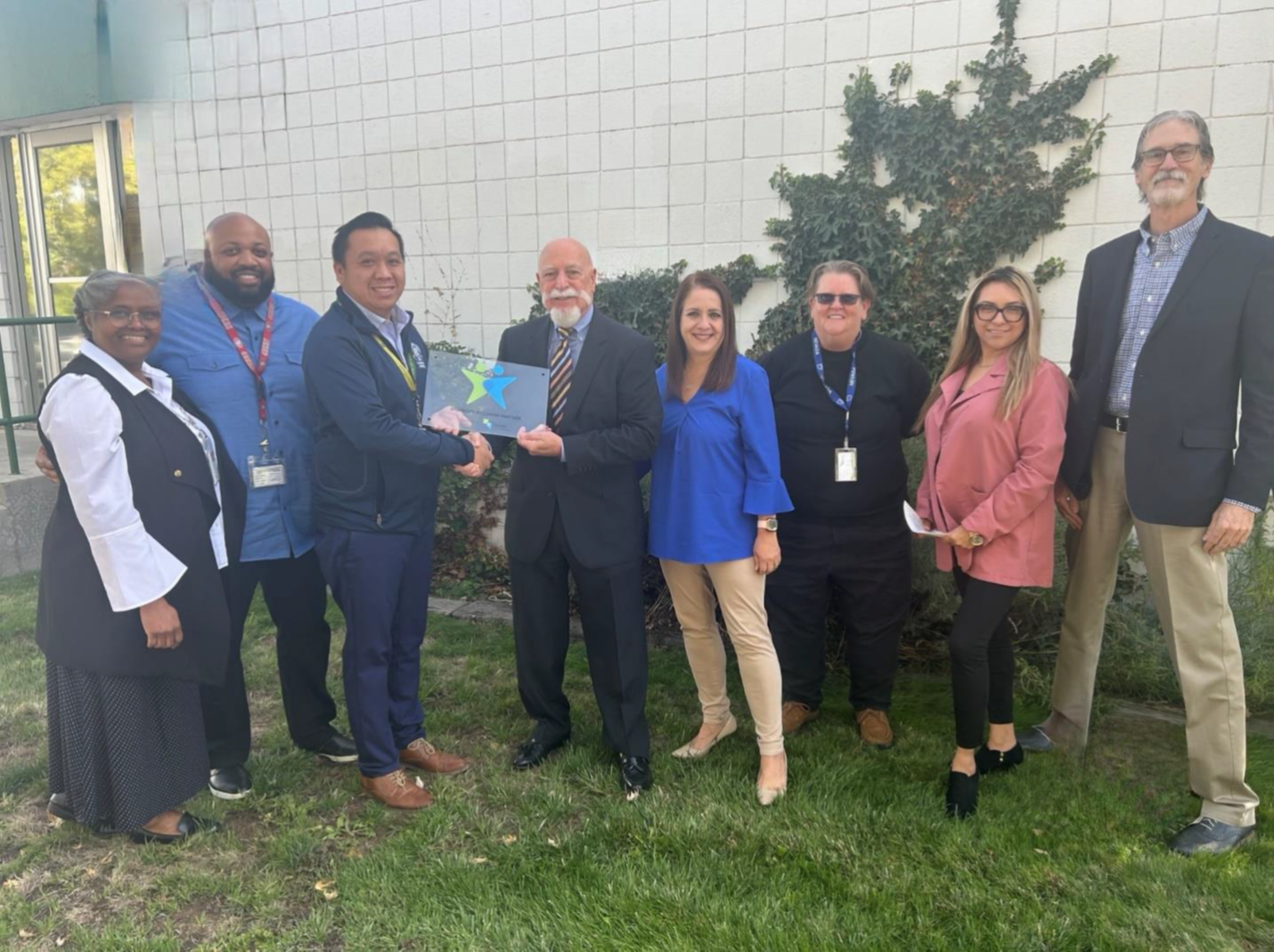 a diverse group of washoe county school district employees smile as they pose with vocational rehabilitation representatives and their plaque