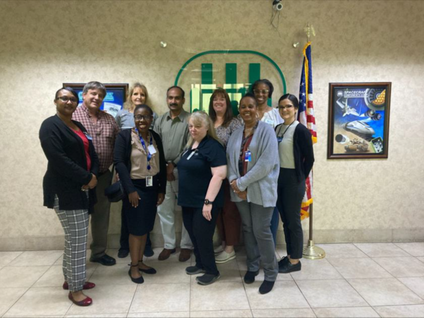 a diverse group of Spacecraft Components management smile as they pose with vocational rehabilitation representatives and their plaque