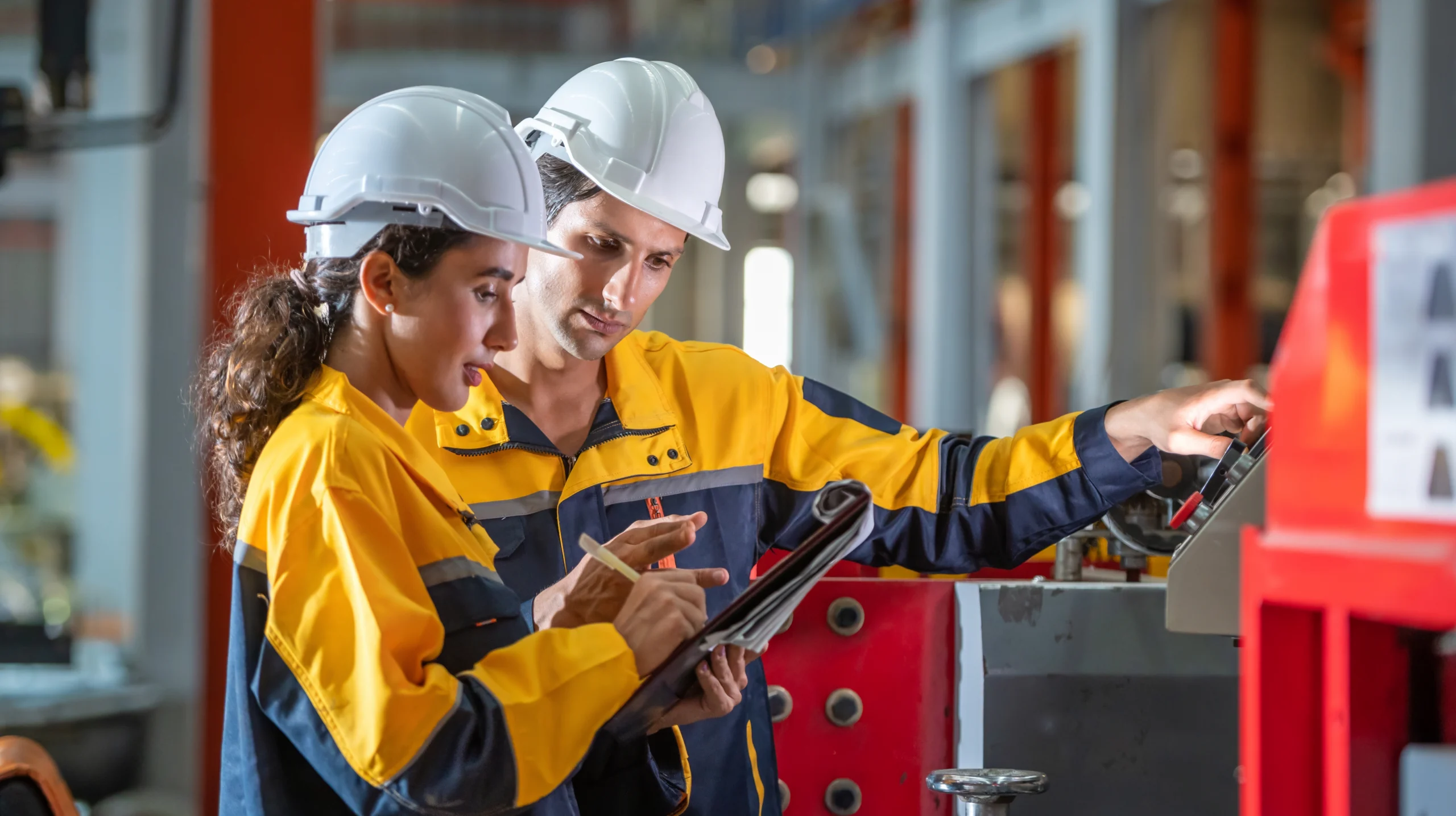 a man and woman wearing white hardhats review a clipboard in a factory